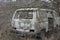 One old white wrecked minibus car overgrown with gray dry vegetation