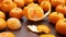 One peeled fruit in centre of many scattered tangerines on brown wooden table