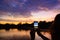 One person photographing Angkor Wat main facade silhouette at dawn holding smart phone. World famous temple mass tourism in