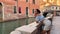 one person, a woman 30 years old in a blue top. leaning on a brick wall, she looks at the Venetian canal. She is