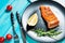 One piece of baked salmon with lemon on a black plate. Blue wood background