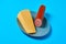 One piece of cheese in form of triangle near half of long sausage on gray round plate lies on blue desk on kitchen or market