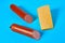 One piece of cheese in form of triangle near two halves of long sausage lies on blue desk on kitchen or market