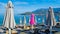 One pink beach umbrella among the rest of grays. Large beach umbrellas over sun loungers on pebble beach