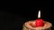 One red candle in wooden candlestick is burning on black background