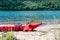 One red colored kayak stranded on the small Island`s beach. Red life jacket and a paddle, grass strows at the left and right