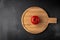 One red and fresh raw tomato in the middle of a round wooden serving plate. dark black and gray textured background, top view.