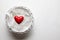 One red heart and feathers in white basket on plastered background