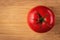 One red and ripe raw tomato in the middle of a wooden cutting board. Textured background with minimalistic still life composition