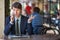 One relaxed young handsome professional businessman working with his laptop, phone and tablet in a noisy cafe.