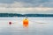 One seagull bird standing resting on an orange buoy on a lake.