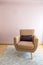 One-seater armchair with cushion on light blue carpet, wooden floor and pastel pink wall.