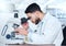 One serious young male medical scientist sitting at a desk and using a microscope to examine and analyse test samples on