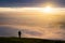 One single anonymous man standing on mountain alone watching sunrise silhouetted stood high above the clouds