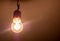 One single old plain bright incandescent lightbulb on in a darkened room, object detail, closeup, from below Bright yellow light