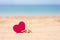 One small  seashell and pink heart lie on a sandy beach.