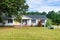 One story small residential home with board siding on the facade. With a large lawn and a tree