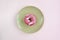 One tasty pink glazed doughnut on beige round plate on pink background. Top view of appetizing donut. Copy space.
