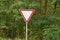 One triangular road sign on a pillar give way against a background of green vegetation