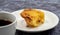 One uneaten Pastel de nata or Portuguese egg dessert on a white plate. Pastel de Belm is a small pie with a crispy puff