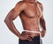 One unrecognizable African American fitness model posing topless with tape measure around his waist while looking