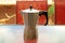 One Used Retro Moka Pot Isolated on the Table with Blurred Red Chair in Background