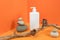 One white blank cosmetic bottle with dispenser, rocks, wooden stick with dried flowers in corner space on orange background.