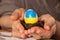 One white chicken egg with a painted flag of Ukraine in a straw basket in the hands of an old woman, culture and holidays , stop