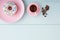 One white donut or doughnut in a pink plate, cappuccino in a pink coffee cup and coffee beans on blue wooden table