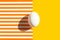 One white egg on duotone yellow orange and white striped background. Easter concept. Hard light harsh shadow. Trendy minimalist