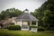 One white gazebo surrounded by a bench and green trees on a cloudy day