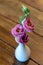 One white small mini vase with pink flower on wooden table