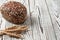 One whole loaf of rye bread with seeds of sunflower near spikelets of wheat lies on weathered white wooden table