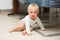 One year old baby boy sitting on floor at home and looking at camera. Little blond kid is crawling on all four under chair