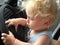 A one-year-old boy with magnificent blond hair in a summer T-shirt sits in the car in the driver`s seat and pretends