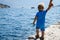 One year old child stands on the edge of the pier and looks at the Bay of Kotor in Montenegro, view from the back