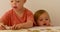 One-year-old child watching how three-year-old playing with puzzle