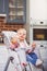 One year toddler girl sits on baby high chair with feeding bottle in her hand.