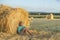 One young boy sits at a haystack in a field on a sunny day and thinks about something