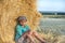 One young boy sits at a haystack in a field on a sunny day and thinks about something