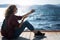 One young girl a woman in a mask and sunglasses sits on a wooden pier on the seashore with a smartphone in her hands. video call.