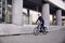 One young man, 20-29 years old, wearing suit, looking smiling. riding, pedaling standing, fancy bicycle. full length body. modern