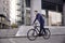 One young man, 20-29 years old, wearing suit, looking smiling. riding, pedaling standing, fancy bicycle. full length body. modern