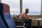 One young man using his laptop or computer pc on a ship traveling in the water of the sea or ocean - man looking outdoor while