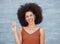 One young mixed race business woman with an afro standing outside against a grey wall and gesturing the peace sign with