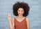 One young mixed race business woman with an afro standing outside against a grey wall and gesturing the peace sign with