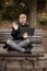 One young relaxed and smiling man, sitting casually on bench with crossed legs in public park, using laptop with video call