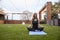 One young woman,20-29 years old, doing yoga while sitting in a sukhasana pose in a beautiful backyard