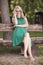 One young woman, 25 years old, sitting in wood bench in park, green dress, looking to camera. full length shot, barefoot