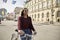 One young woman, looking forward, pushing her bicycle in city, pedestrian zone European old architecture style